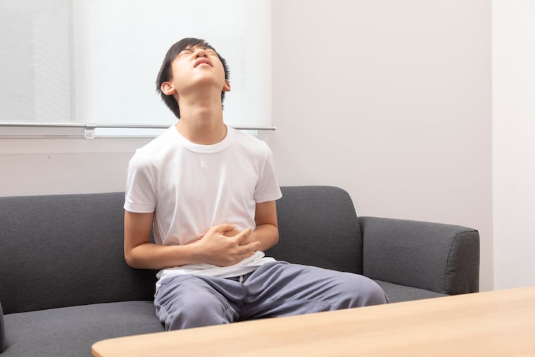 Teen boy suffering from stomachache sitting on sofa at home.