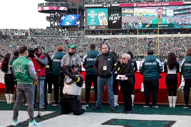 Ivan Glubish (left), who is pictured on the video screen in the background, plays the national anthem on the saxophone before the Eagles and Packers played their wild-card game on Sunday.