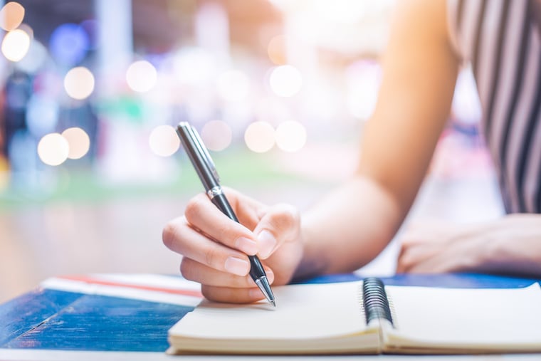 Woman's hand writing on a notebook with a pen on a wooden desk.Background blur backlight