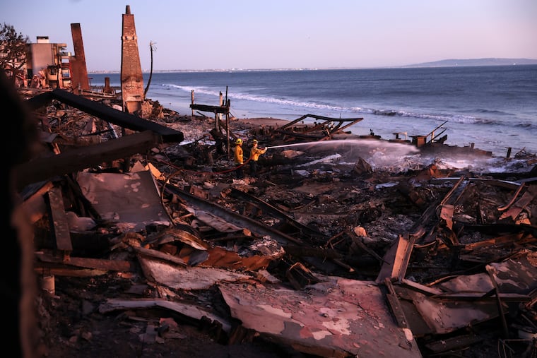 Los Angeles Fire Department's Dylan Casey and Mike Alvarez work on extinguishing a hot spot in the aftermath of the Palisades Fire along the Pacific Coast Highway in Malibu, Calif., on Sunday, Jan. 12, 2025. 