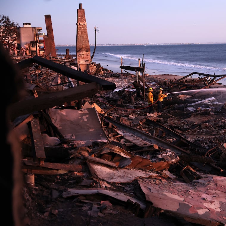 Los Angeles Fire Department's Dylan Casey and Mike Alvarez work on extinguishing a hot spot in the aftermath of the Palisades Fire along the Pacific Coast Highway in Malibu, Calif., on Sunday, Jan. 12, 2025. 