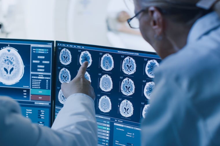 In Control Room Doctor and Radiologist Discuss Diagnosis while Watching Procedure and Monitors Showing Brain Scans Results, In the Background Patient Undergoes MRI or CT Scan Procedure.